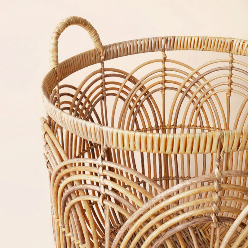A close up of a round wicker laundry basket, showing its handwoven pattern as well as arched handle. 