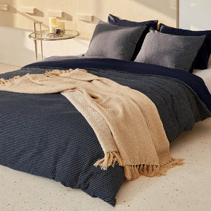 The brown throw with herringbone pattern drapes elegantly on a bed which covered by navy blue covers.