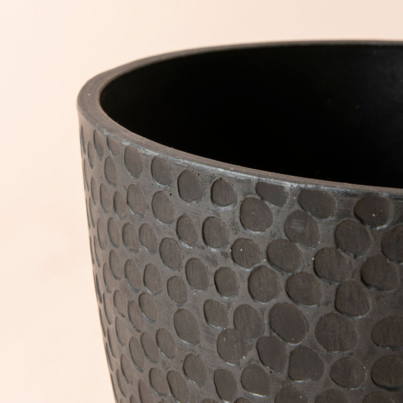 A close up of black plastic planter, showing a unique honeycomb pattern on its exterior.