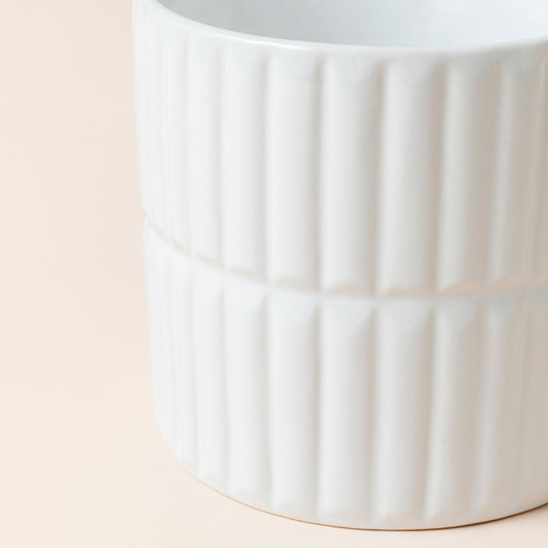 A close up of bright white planter, showing its fully glazed body and ribbed design.