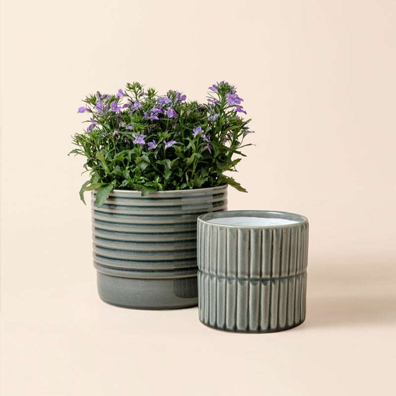 A set of two gray pots with tidy lines, one of which holds flowers.