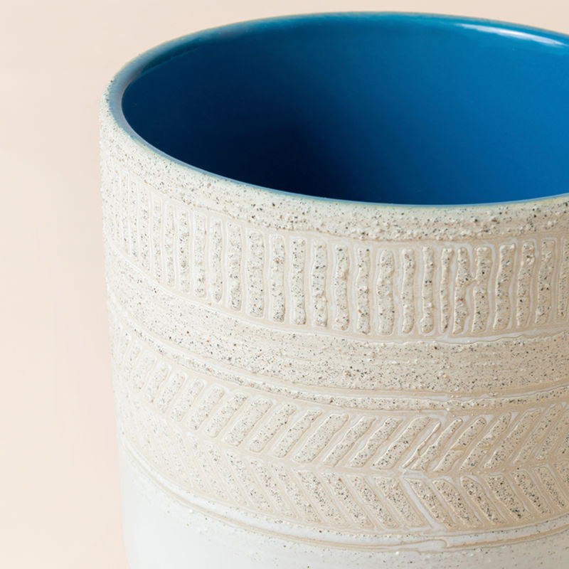 A close up of ivory white planter, showing a ribbed herringbone pattern around its grainy exterior.