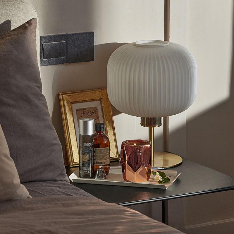 A burning candle is displayed on a black bedside table, surrounded by home decorations.