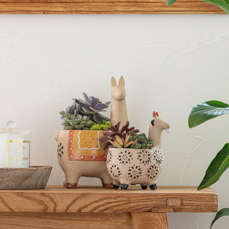 A set of two animal shapes planters are displayed on a wooden cabinet holding plants with them, next to a jar of candle.
