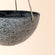 A close up of light gray hanging pot, showing its sturdy rope and concrete texture.