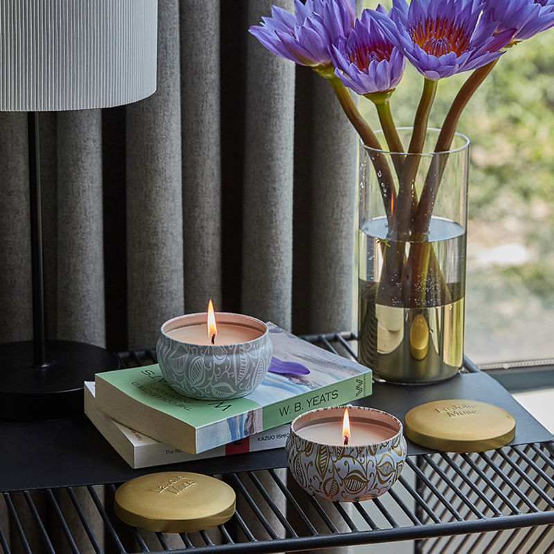 A pair of burning candles are displayed on a iron frame bedside table, accompanied by a vase of tulips.