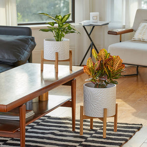 The large lumen white planter is placed on a carpet in the living room, next to a table.