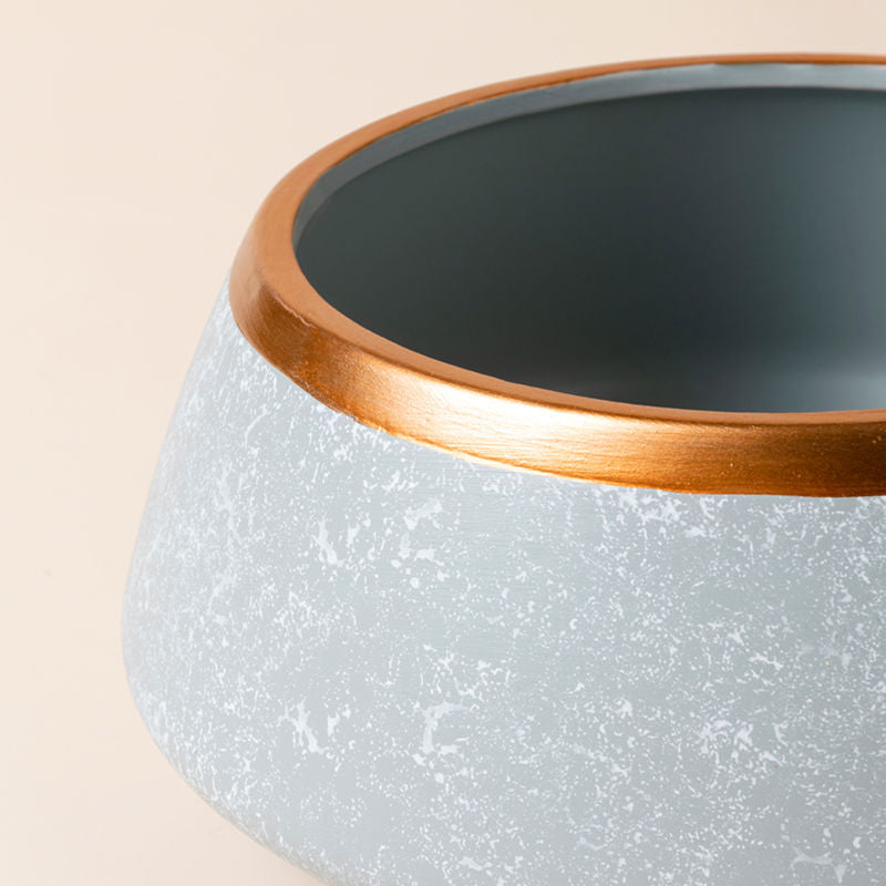 A close up of light gray pot, showing its marble-like pattern and metal textured rim.