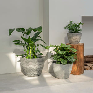 Three grey pots are placed in a staggered way. The small one is displayed on a wood column, shadows on the wall are in the background.