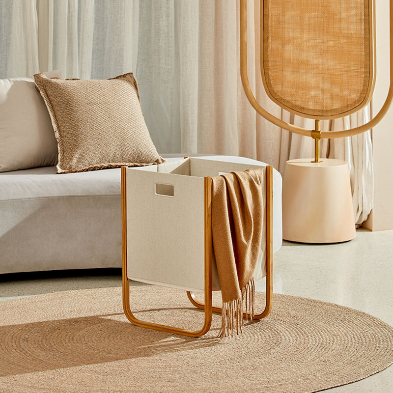 A off-white bamboo basket is placed on a round carpet with a blanket on the edge of it.
