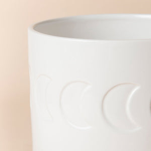 A close up of white ceramic planter, showing a beautiful moon pattern around its exterior.