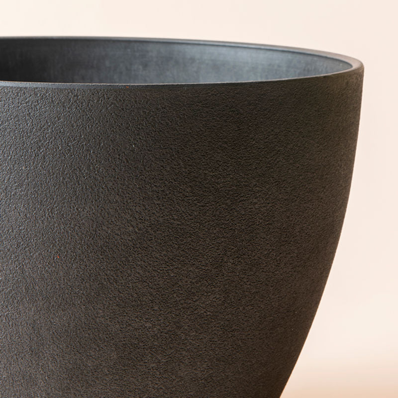 A close up of black outdoor planter, showing its concrete textured exterior and sphere-shaped body.
