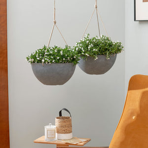 A set of two gray pots with flowers in them are hanging on the wall, above the wooden coffee table.