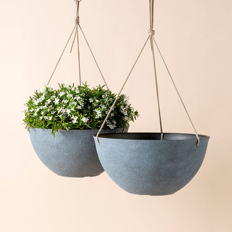 A set of two gray planters are hanging on the wall one of which holds flowers.