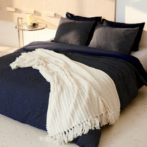 A contrast of the off-white chenille throw being placed on a dark color bed.