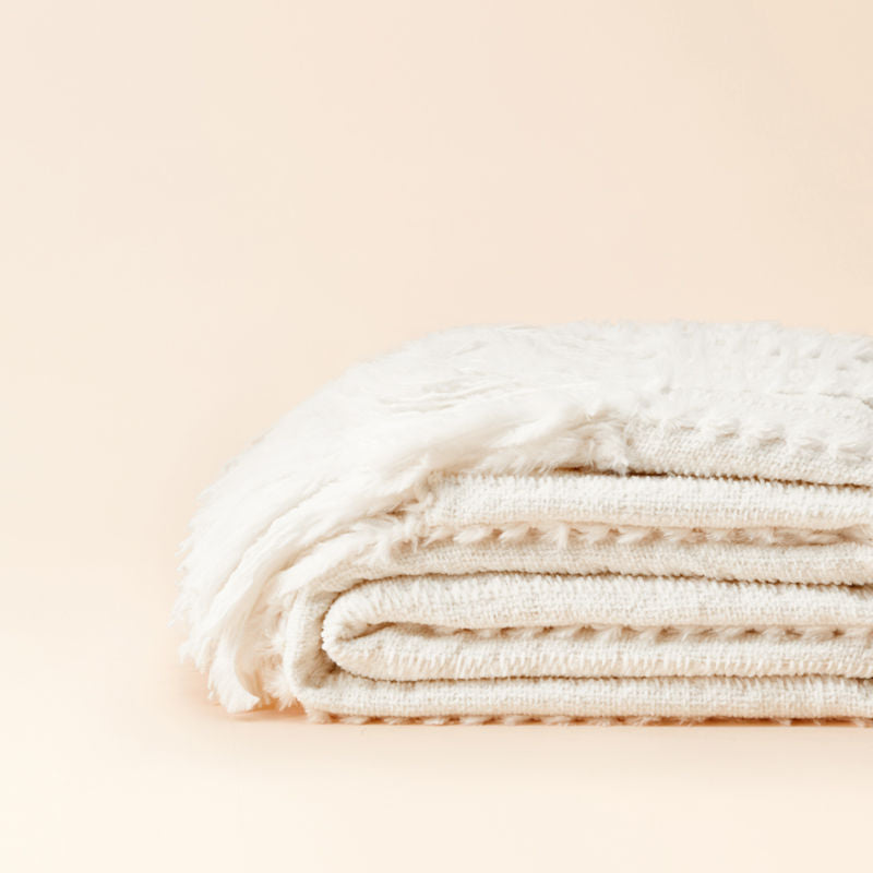 A folded chenille throw blanket in the off-white color, made softly to mimic fluffy rabbit fur.