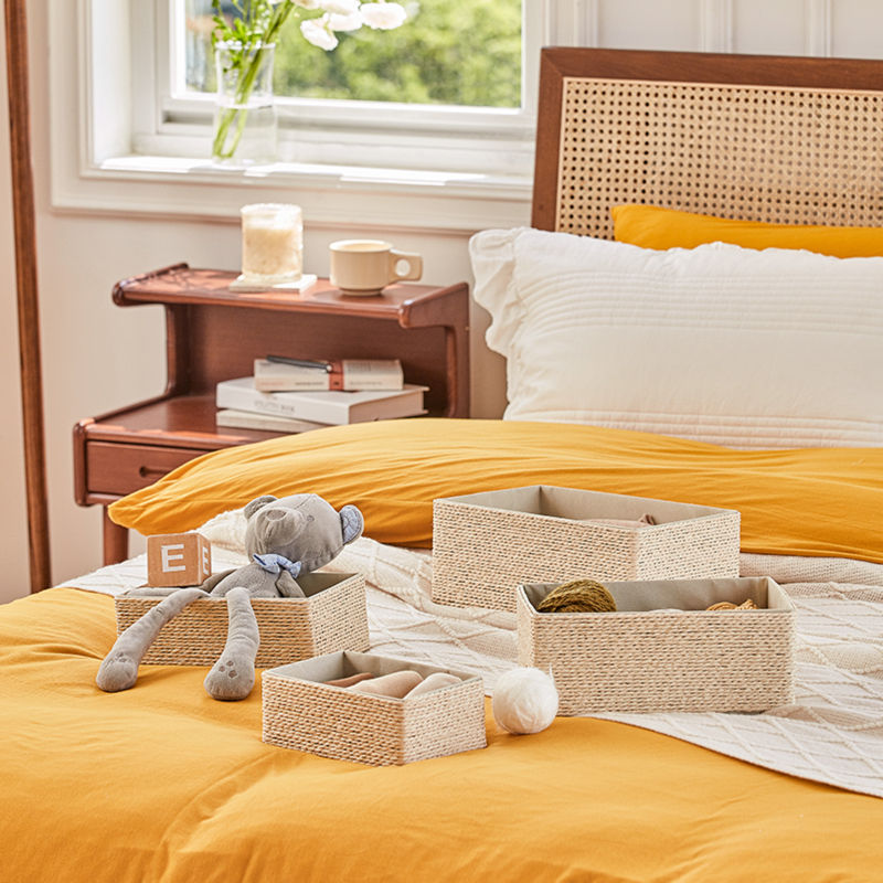 Four different sizes of storage baskets storing toys and balls of colored yarn are displayed on a bed.