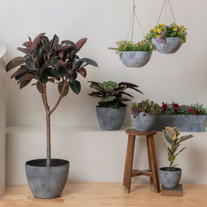 Seven gray planters in different sizes and shapes are displayed against a white wall, including a pair of hanging pots.