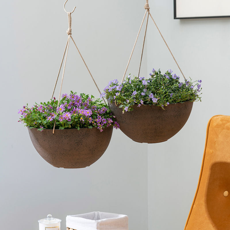 A pair of rusty pots are hung above a yellow sofa, both potted with small purple flowers.
