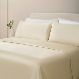 Sofia Ivory White Double Satin Stitched Cuff 300 thread count cotton bed sheet set. Ivory pillows and ivory cotton sheets on bed next to side table and plant.