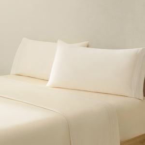 Sofia Ivory White Double Satin Stitched Cuff 300 thread count cotton bed sheet set. Ivory pillows and ivory cotton sheets on bed from side angle.