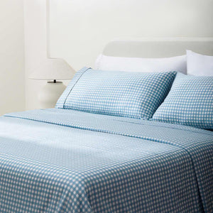 Paulina Blue Check Picot Edge 200 count cotton sheet set. White and blue gingham pillows and white and blue gingham sheets on bed with side table and lamp from side angle.