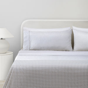 Paulina Pewter Check Picot Edge 200 count cotton sheet set on a fully made bed. White and gray gingham duvet and two white pillows and two white and gray gingham pillows next to side table with lamp.