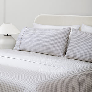 Paulina Pewter Check Picot Edge 200 count cotton sheet set. White and gray gingham pillows and white and gray gingham sheets on bed with side table and lamp from side angle.