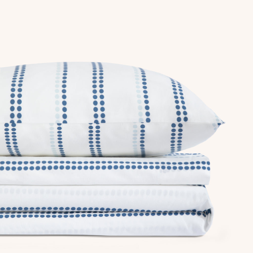 Camille Blue Stripe bed sheet set. Single dotted blue and white dotted pillow stacked on folded blue and white dotted sheet set.