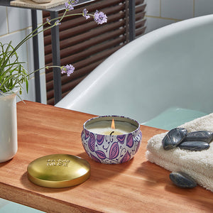 A burning candle, a pot of tulip and some bath supplies are placed on a wooden board set across a white bathtub.