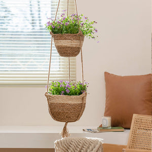 A set of two rope planters are hanging on the wall together with plants in them. Planters are displayed in front of a window.