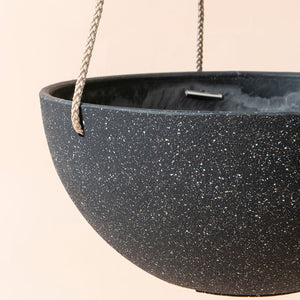 A close-up of the black planter, showing its speckled pattern and plastic features.