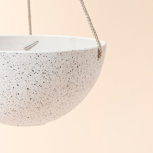 A close up of white hanging pots with speckles, showing its sturdy rope and bowl shape design.