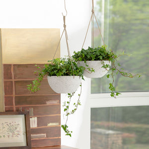 A pair of white speckled planters are hung in a bright room with sturdy ropes.