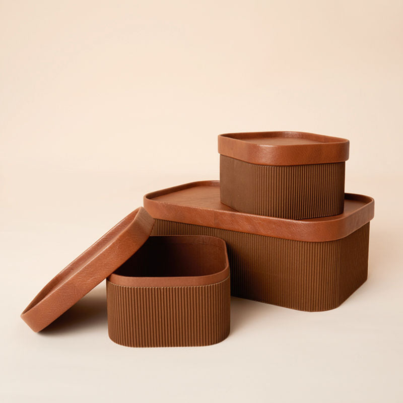 A set of three chocolate brown storage baskets with lids in different sizes.