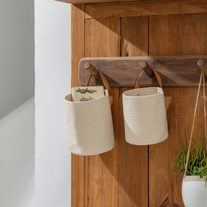 Two beige round baskets are hanged on a wooden gate with a pot of green plants.