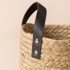 A close up of tote water hyacinth basket, showing its leather handle and woven pattern.