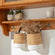 A pair of tote hyacinth baskets are hung on a wooden shelf against a white wall.
