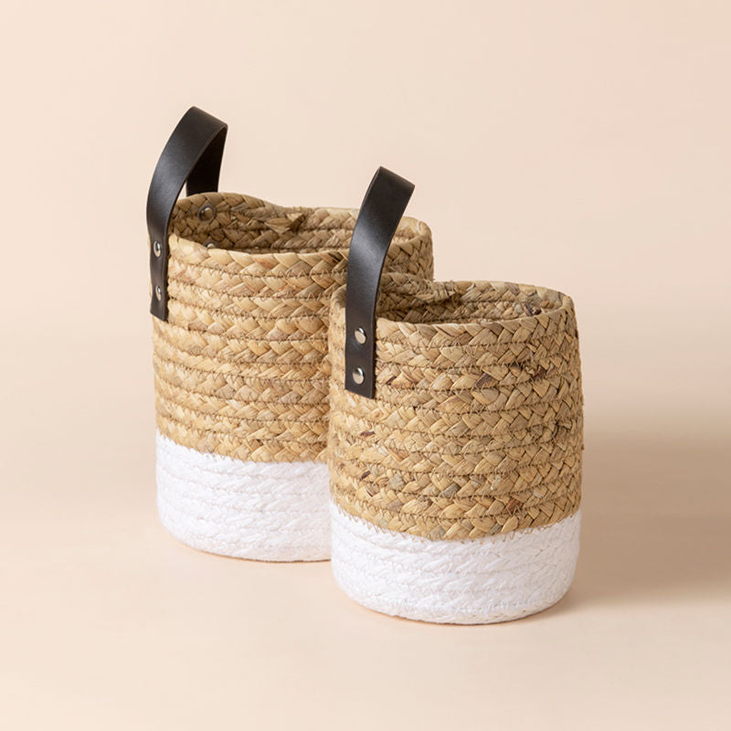 A set of two water hyacinth weaving baskets with white and beige body and leather handles.