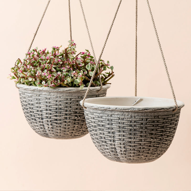 A set of two planters decorated with stone patterns are hanging on the wall with support from ropes.
