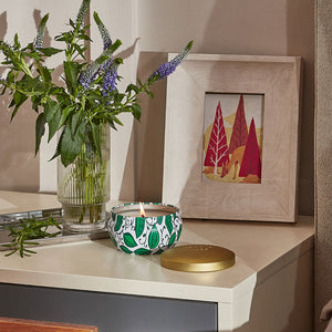 A burning candle is placed on a bedside cabinet with a vase of tulips and a modern art painting.