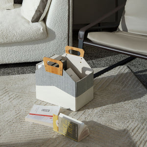 A white and gray storage basket is placed on a square carpet with two books beside.