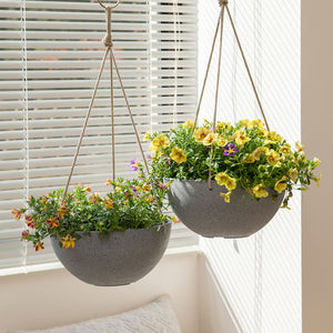 Two weathered gray planters are displayed in front of blinds, both potted with yellow flowers.