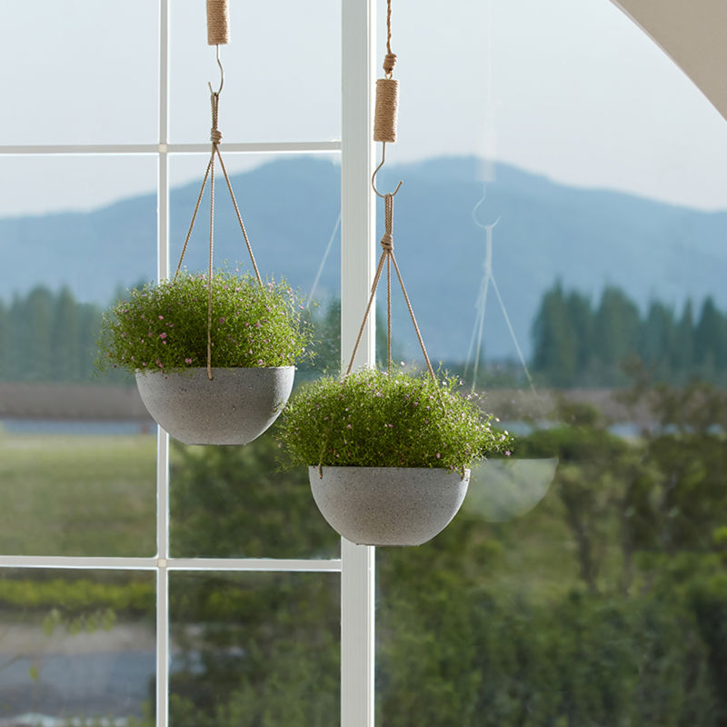 Two gray planters are displayed in front of a window. Outside the window is a green field.