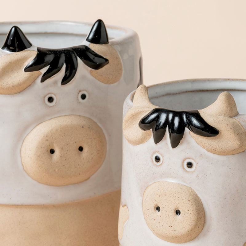 A close up of two white cow pots, showing the details of the head of two cows.