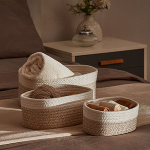 Three white and desert rope baskets are displayed on a bed. Each of baskets contains some household goods.