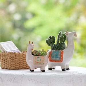 A pair of white goat planters are displayed on a small round table with a rattan basket.