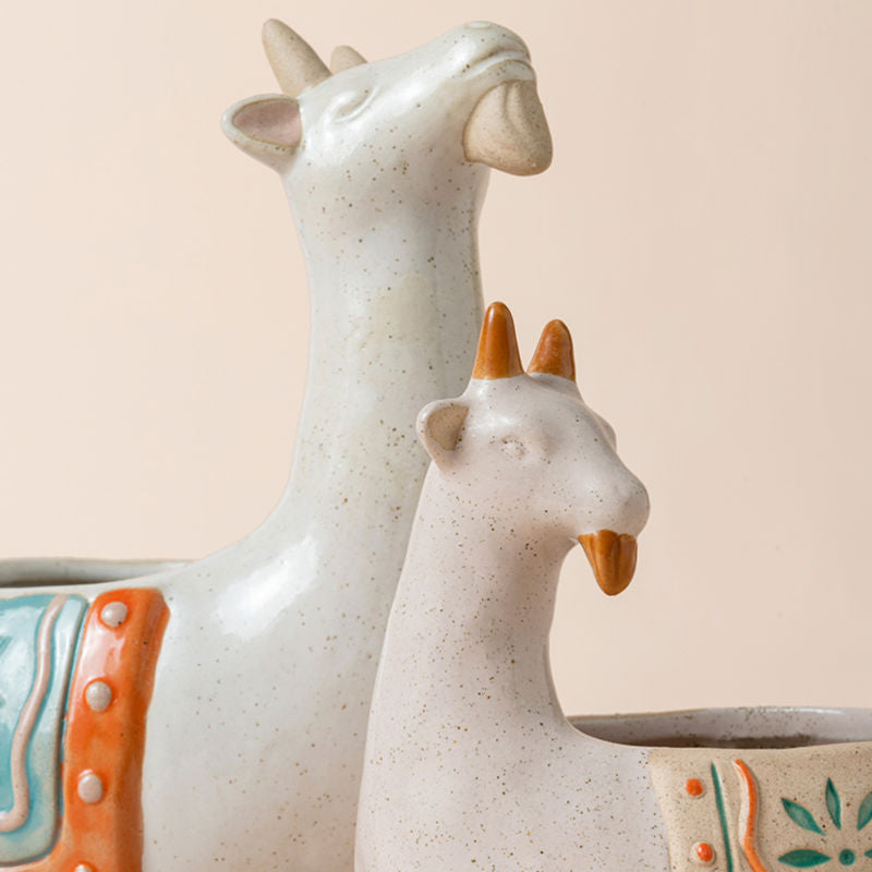 A close view of two white goat planters, showing the details of the heads of both goats.