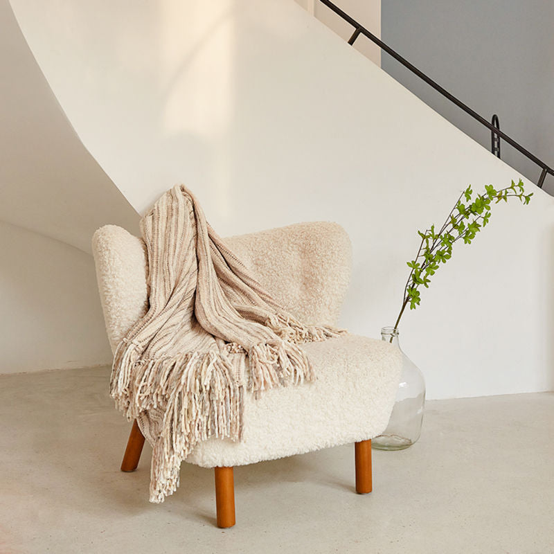 A woven chenille throw blanket is placed on a white-colored couch next to a green plant.