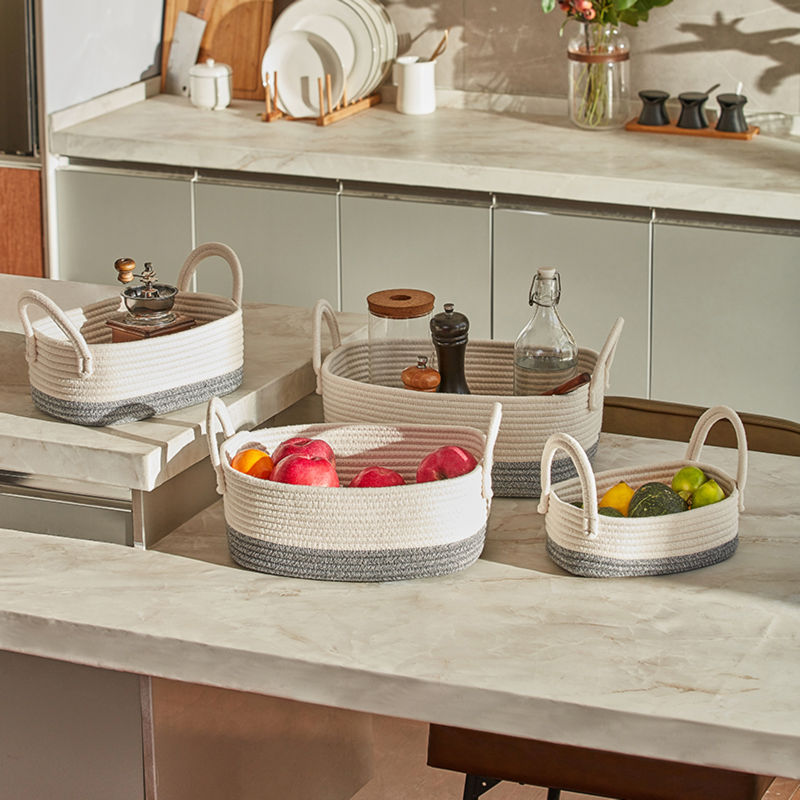 Four cotton rope baskets, filled with fruits and kitchen supplies, are placed on a white marble table in the kitchen.